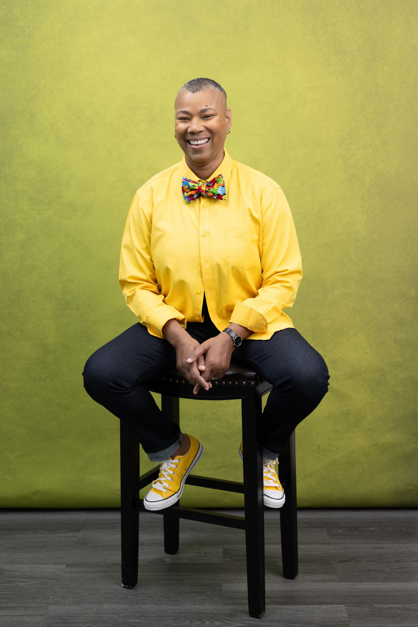 Karen Anastasia Prescod seated and smiling in a yellow shirt and colourful bow tie